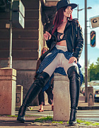 Exhibitionist Jeny Smith, wearing white tights, high leather boots and a black leather jacket, poses for a photoshoot on a crowded street.