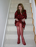 Jamie Lynn, clad in burgundy pantyhose and a red satin robe, stands on the staircase, inviting you to watch as she teases with her bare breasts and seductive gaze