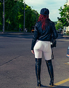 Exhibitionist Jeny Smith, wearing white tights, high leather boots and a black leather jacket, poses for a photoshoot on a crowded street.
